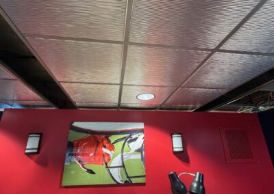 Framed photo on a red wall between two wall sconces, with ceiling panels above and two black lamps in the foreground.