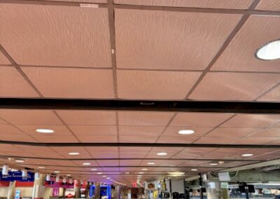 Spacious airport terminal with check-in counters in the distance, empty brown-tiled floor and a grid ceiling with recessed lights.