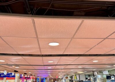 Ceiling with exposed wiring and beige tiles, recessed lights, view of a busy concourse in the distance.