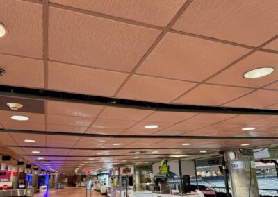 Long indoor concourse in an airport terminal with shops along the right and a grid ceiling above.