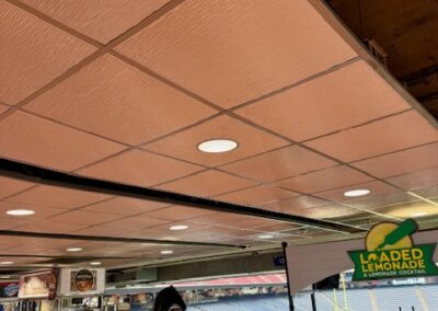 Concession area in a stadium concourse with white counters, coolers, and a bright Loaded Lemonade sign; empty seats visible beyond.