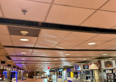 Long indoor hallway with beige tiled ceiling, recessed lights, and snack shops along the right side.
