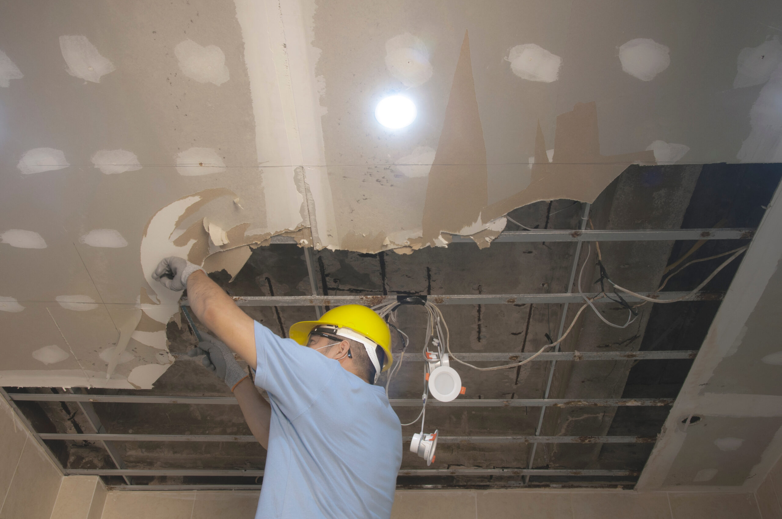 Home renovation worker repairing a water-damaged ceiling, highlighting maintenance work on interior ceiling surfaces.