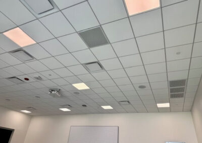 Ceiling view of a white, tiled room with recessed lights and vents; a whiteboard mounted on the far wall.