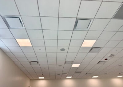 Ceiling with square grid tiles, recessed lights, and vents in a large room or office space.