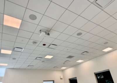 Drop-ceiling conference room with recessed lights, vents, and a ceiling-mounted projector.