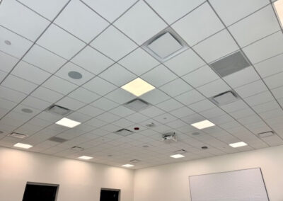 Ceiling with grid of square tiles, recessed lights, vents, and a whiteboard on the right wall in a conference room.